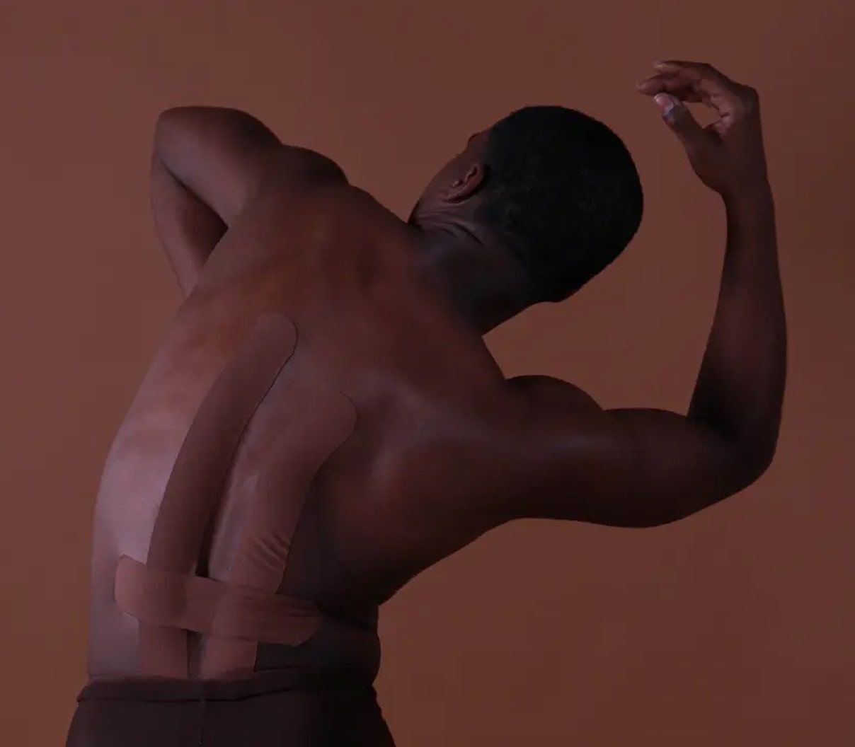 Man posing with arms raised against a brown background