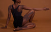 Person wearing a black bodysuit and sheer brown stockings on a brown background