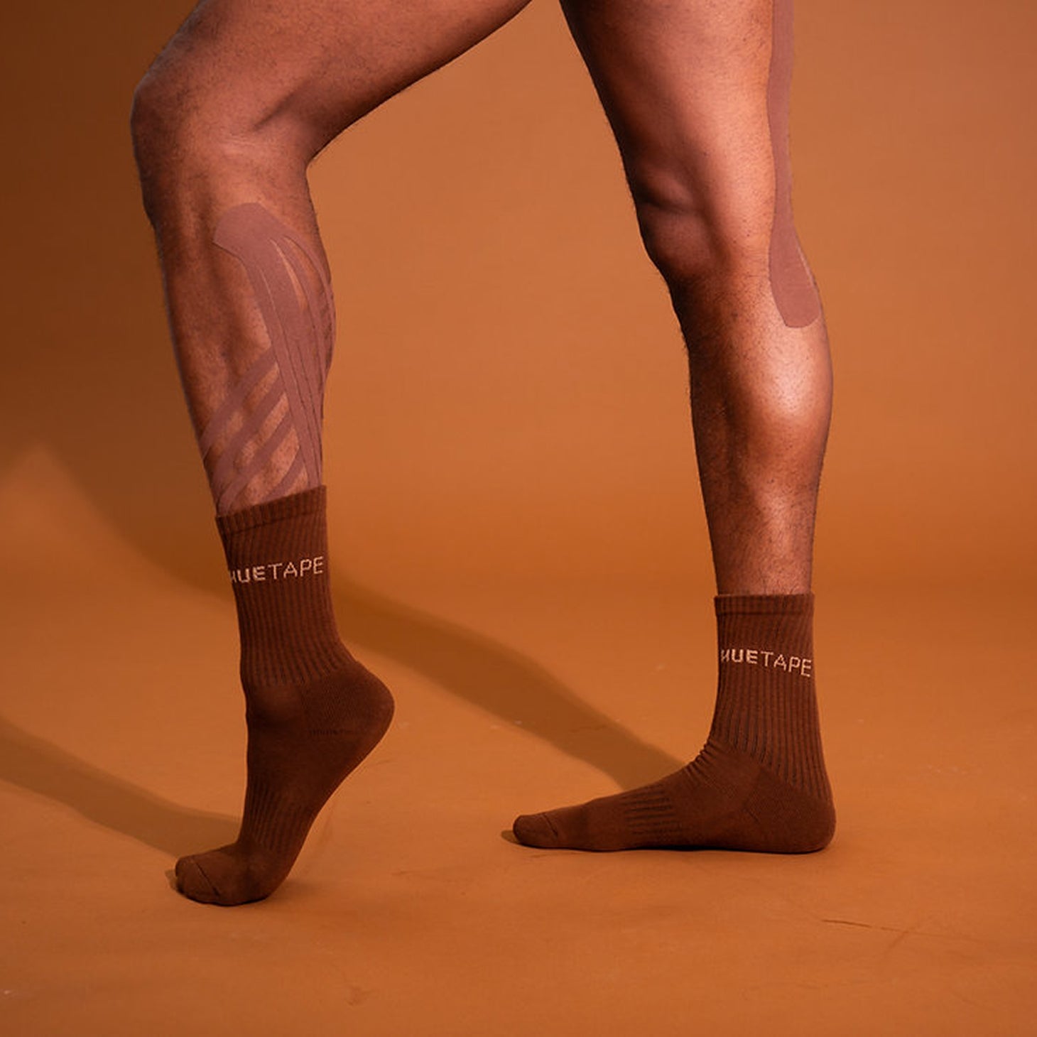 Brown socks with visible branding on a person's legs against an orange background