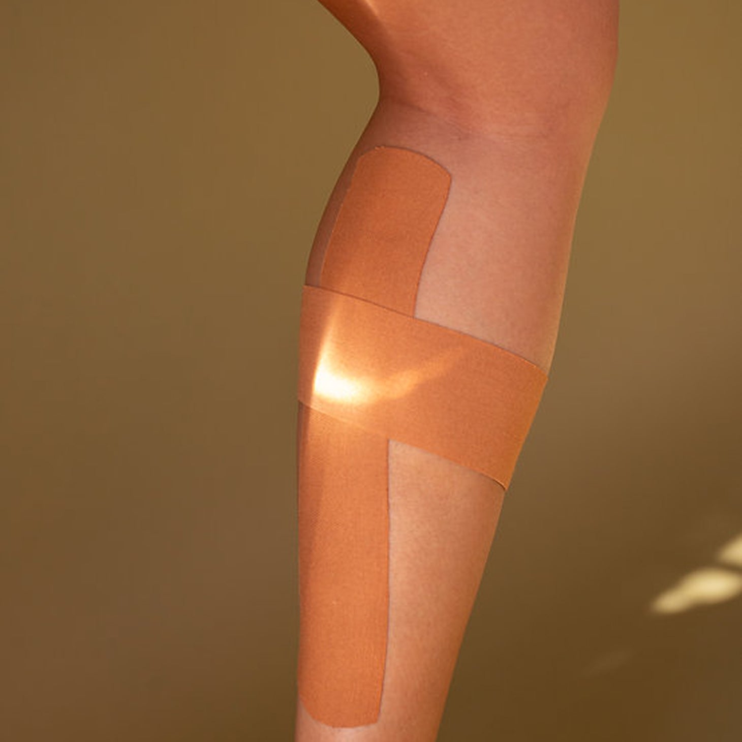 Kinesiology tape applied to a person's leg on a brown background