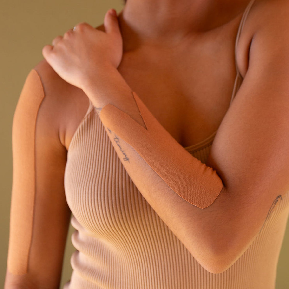 Close-up of a person wearing a beige ribbed tank top against a neutral background