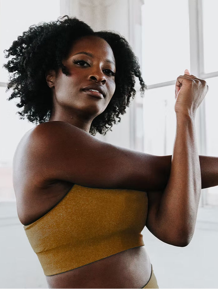 Woman in a mustard yellow top standing indoors with a neutral background