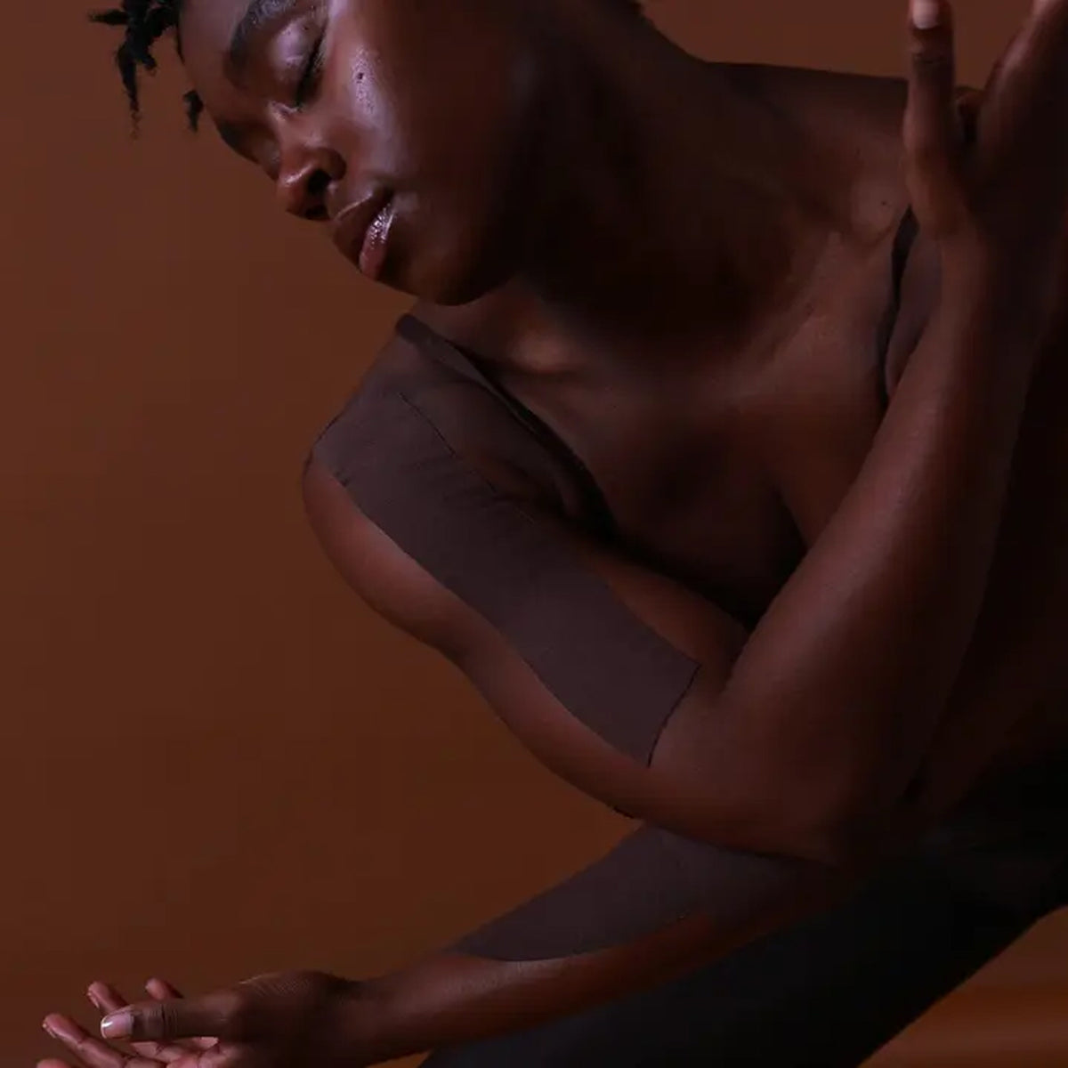 Woman in a yoga pose against a brown background