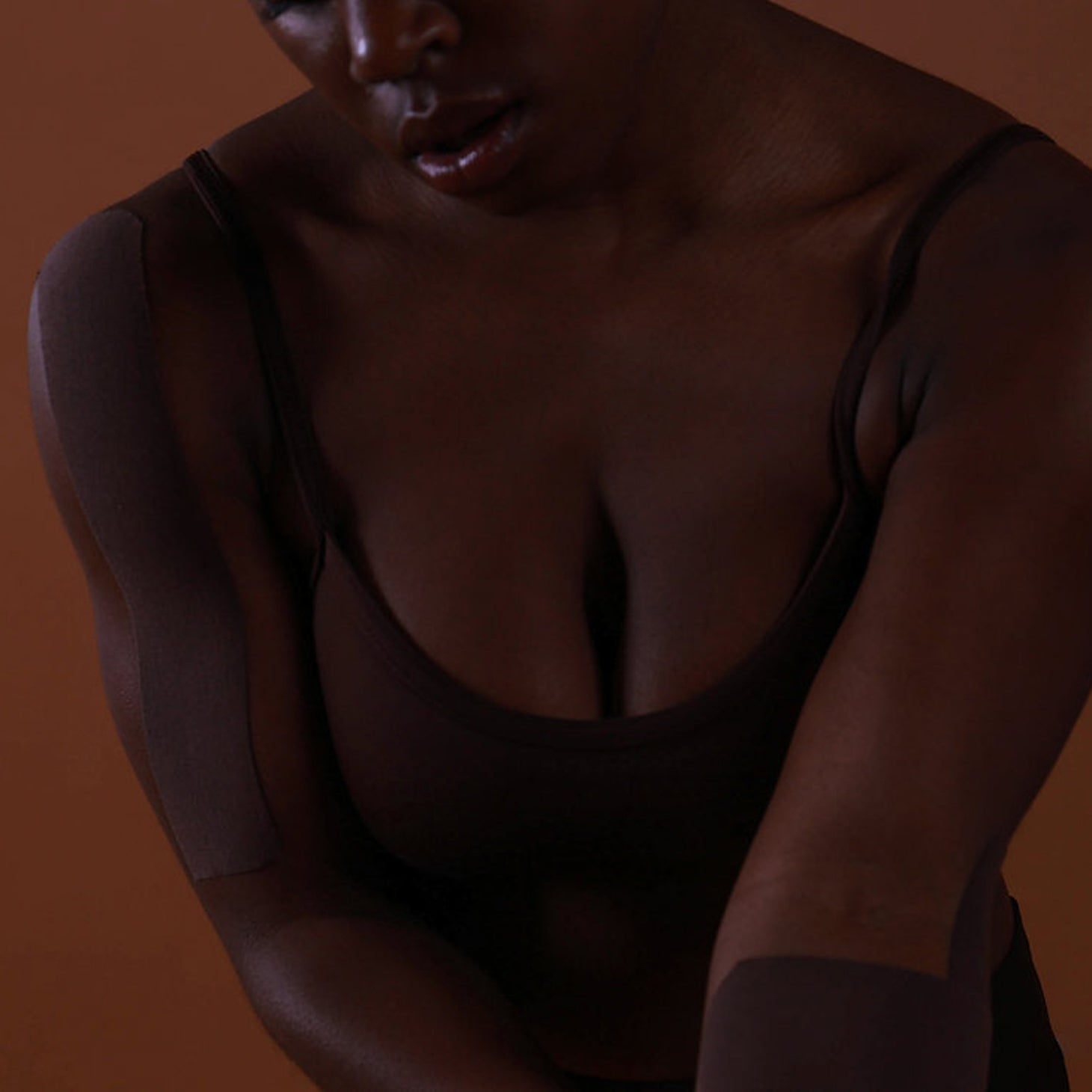 Partial view of a person wearing a dark top against a brown background