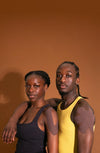 Two people standing close together with kinesiology tape on their shoulders against a brown background