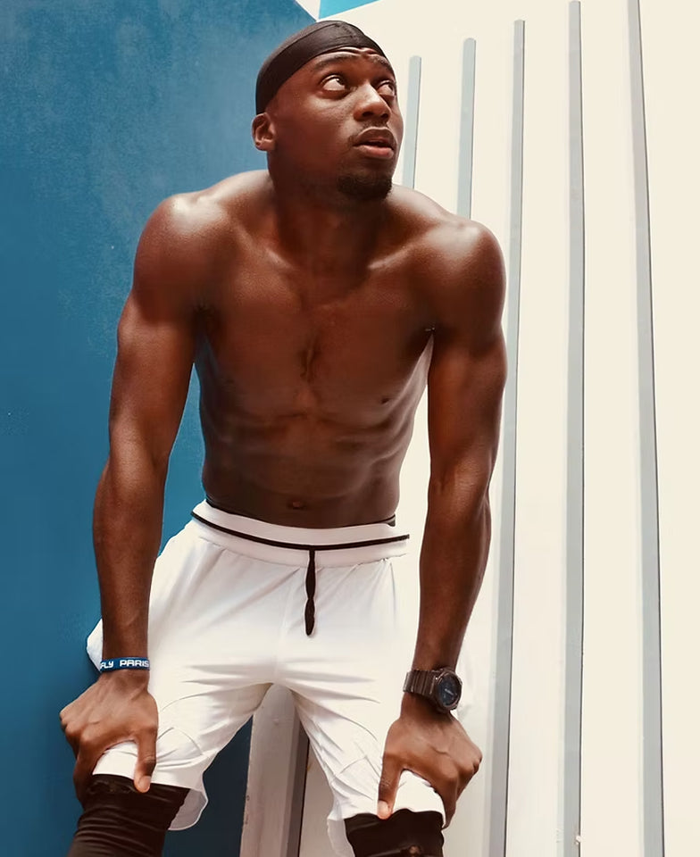 Man wearing white shorts with a black waistband against a blue and white background