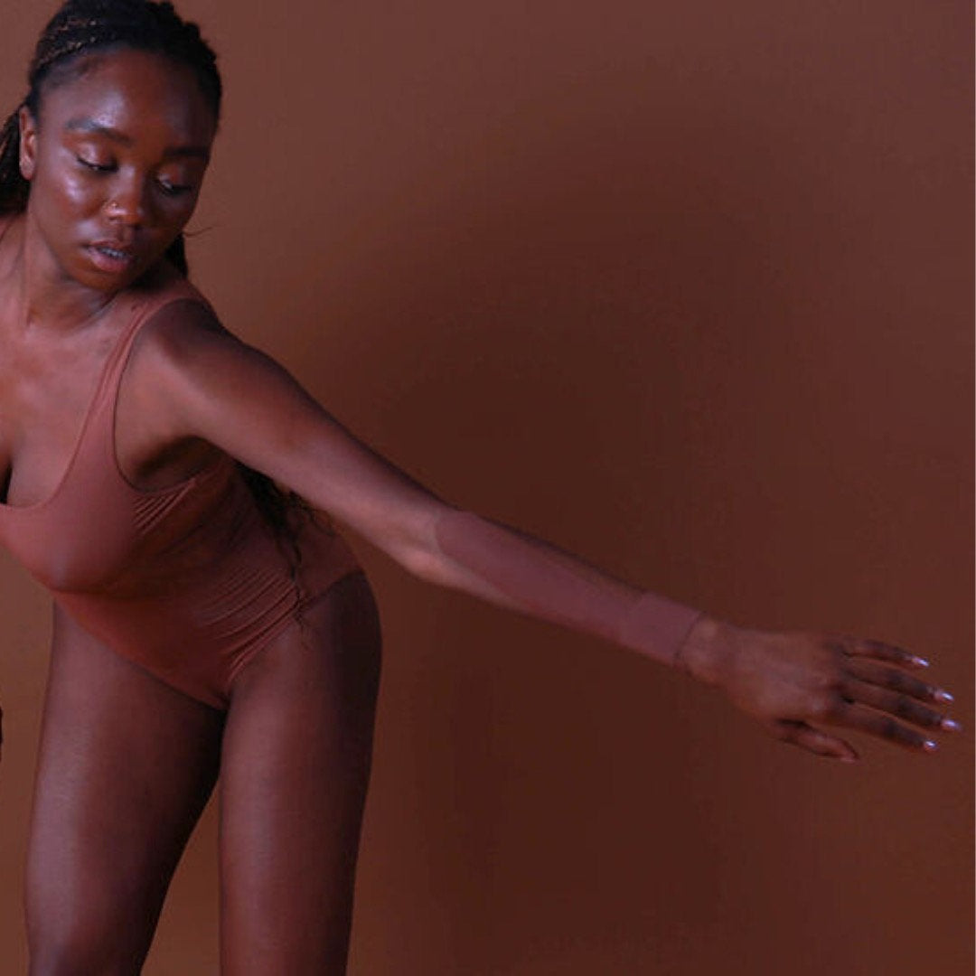 Woman in a brown bodysuit posing against a brown background