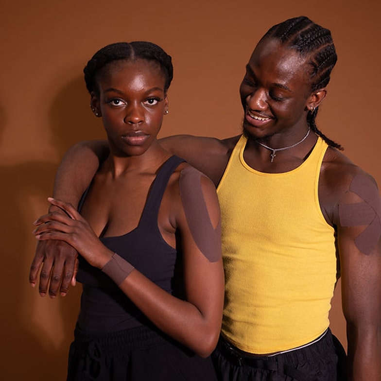 Two women with brown and yellow skin tones standing against a brown background